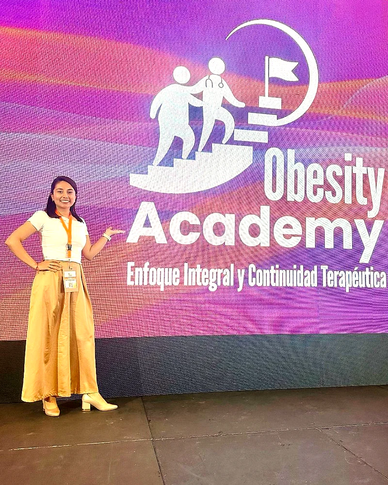 La Dra. Michelle Mejía junto a la pantalla de Obesity Academy: Enfoque Integral y Continuidad Terapéutica